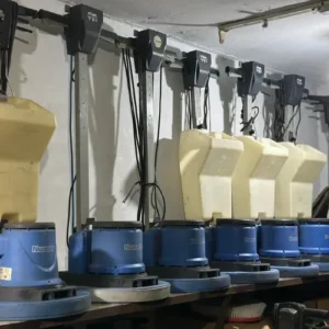 A row of used Numatic single-disc floor scrubbers and polishing machines with water tanks lined up on a shelf, available for sale in Faislabad, Pakistan.